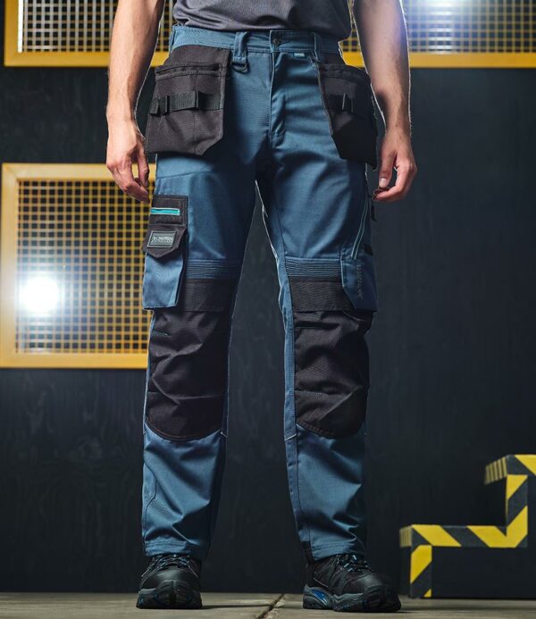 "Slim fit. High shaped back waistband with belt loops and D ring attachments. Inner anti-slip waistband. Zip fly with button and shank button over. Foldaway holster pockets with multiple compartments. Two side pockets. Right hip zip pocket. Reinforced crotch seam. Two multi-function tool and mobile phone pockets on legs with reflective piping. Elasticated panels above knees for ease of movement. Cordura® top loading knee pad pockets. Drawcord hem with reinforced hem overlay. Triple needle stitching. Reflective piping on rear of legs. Branding on left waistband